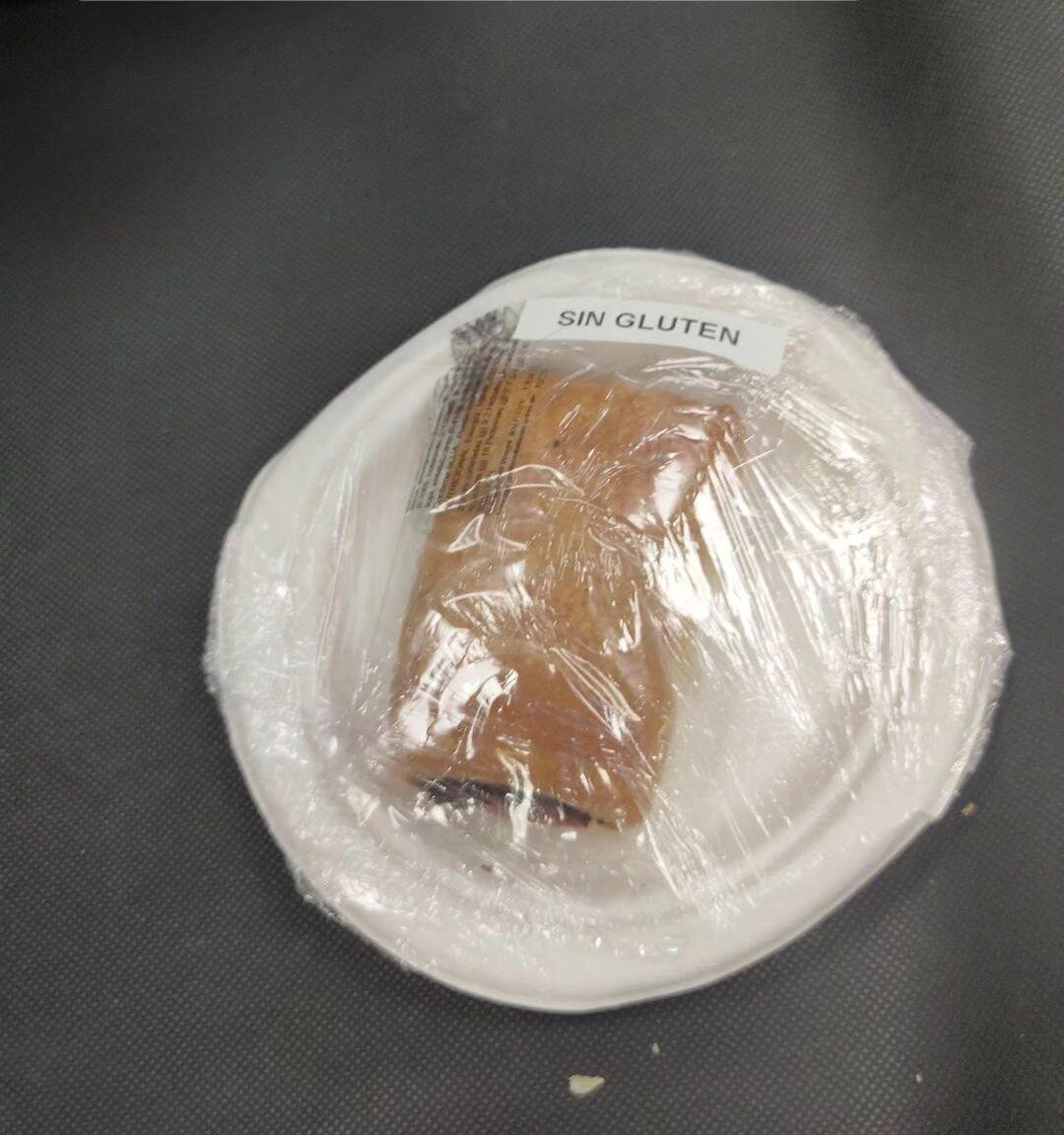 Foto de lo que parece una napolitana de chocolate peusta en un plato de cartón y envuelto en film transparente con una pegatina que reza: sin gluten.